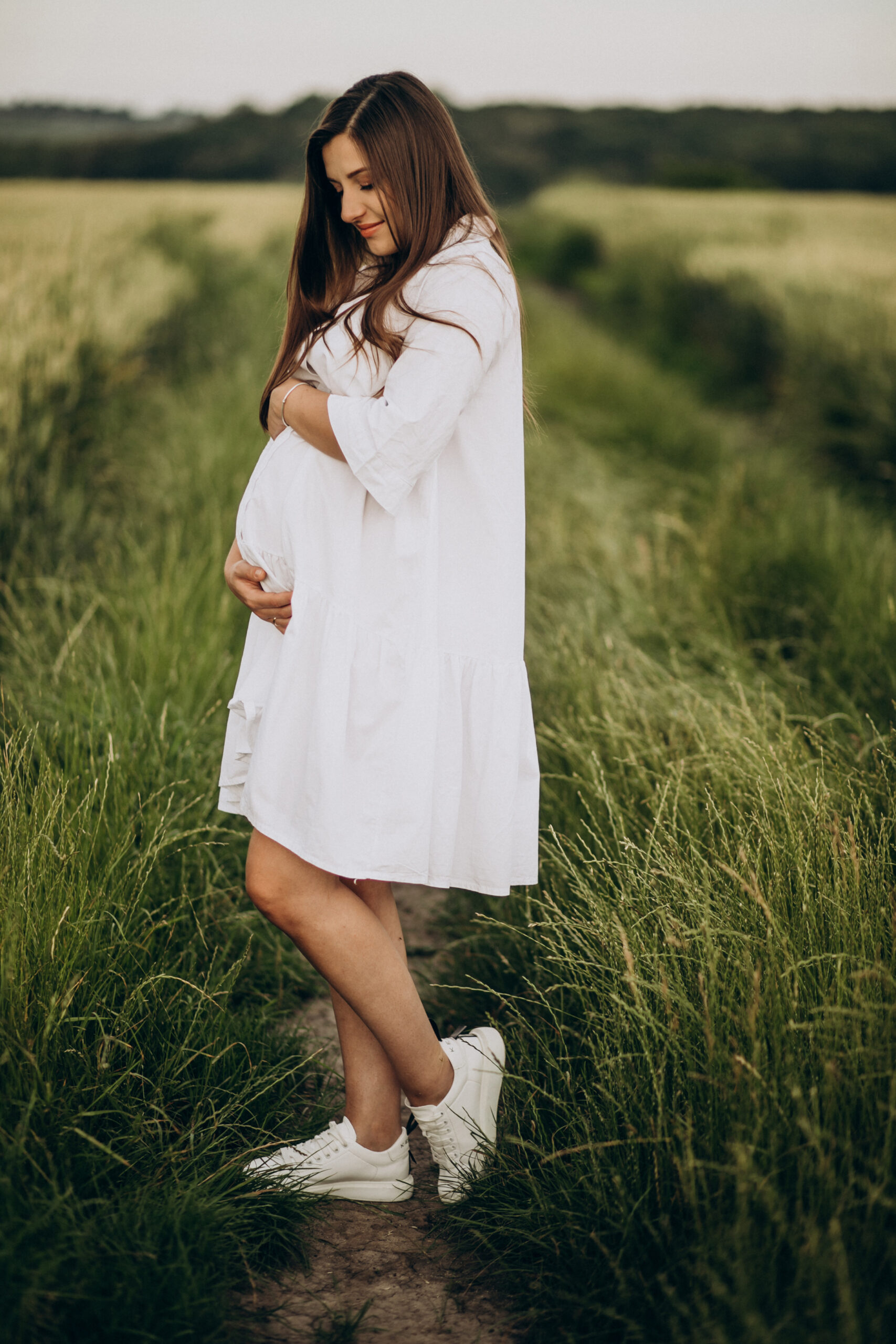 Beautiful pregnant woman standing in a field, embracing her baby bump during maternity journey.